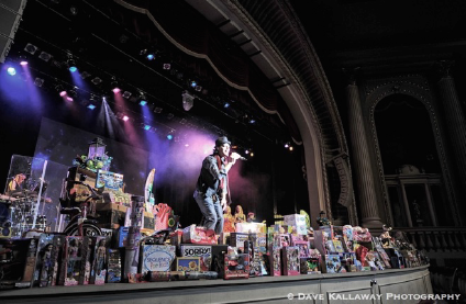 Joe.e onstage with donated toys from the event